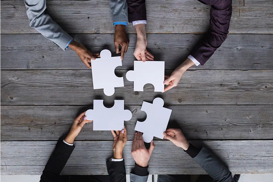 Four business people connect jigsaw puzzle pieces