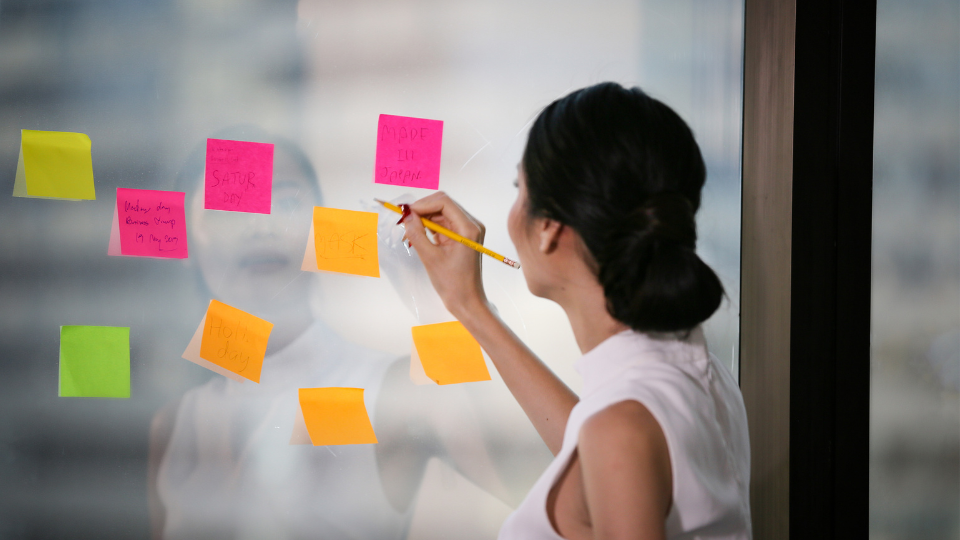 A person writing on sticky notes in front of a window