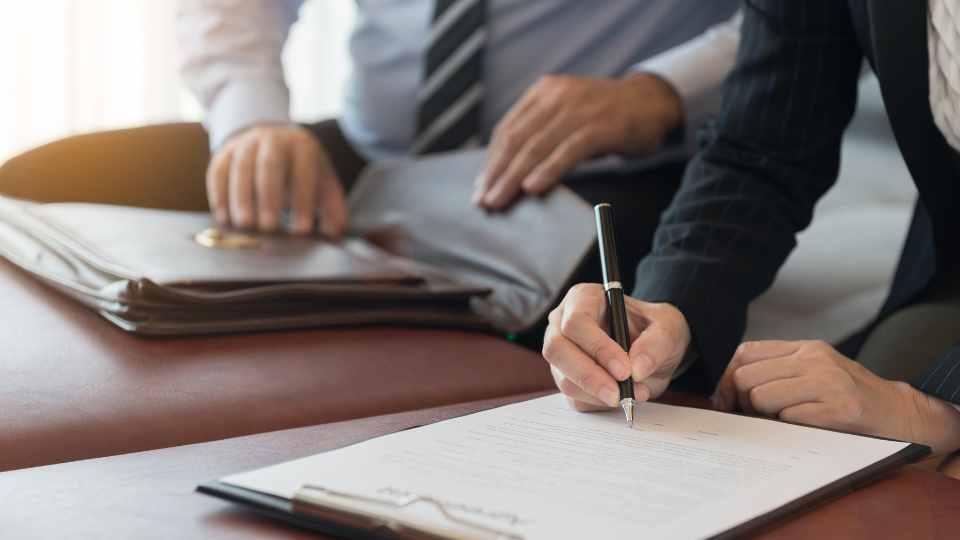 Two people signing documents at a desk 