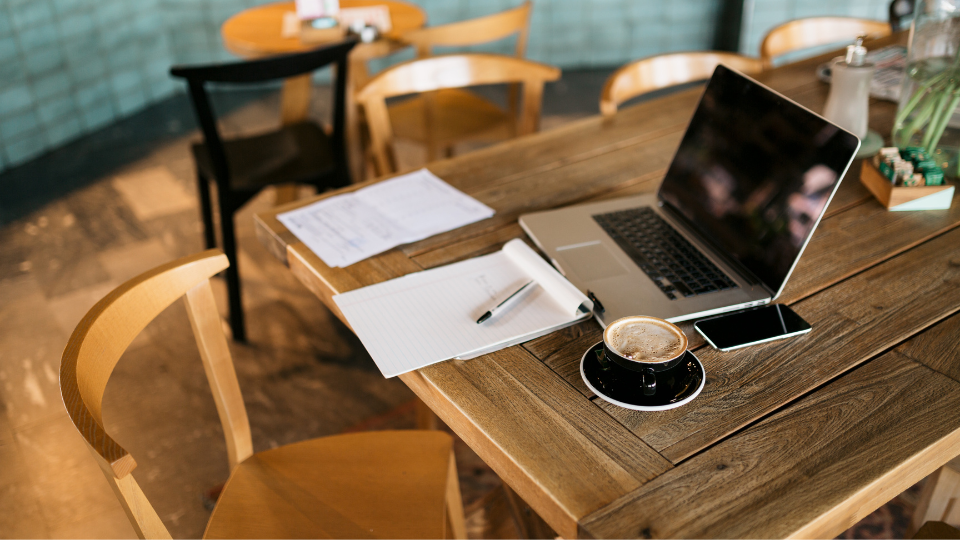 A laptop sitting on a wooden table with a cup of coffee