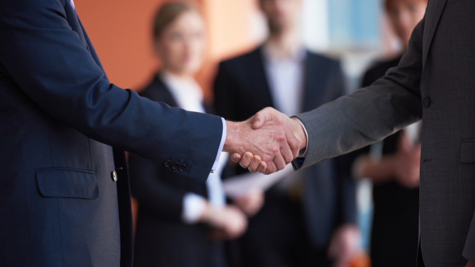 Two business people shaking hands in front of a group of people 