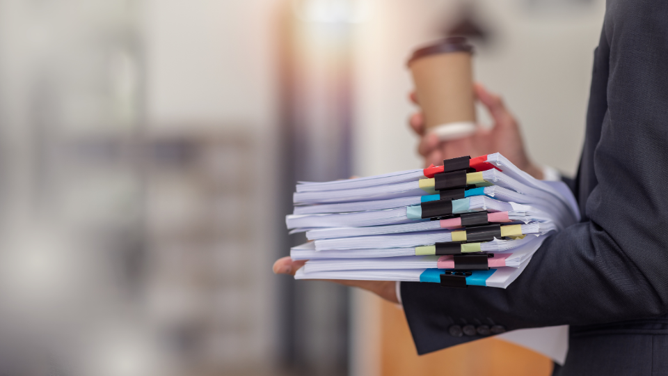 A person in a suit holding a stack of papers and a cup of coffee