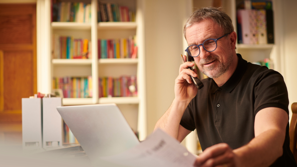 A businessperson sitting at a desk with a laptop and talking on the phone.